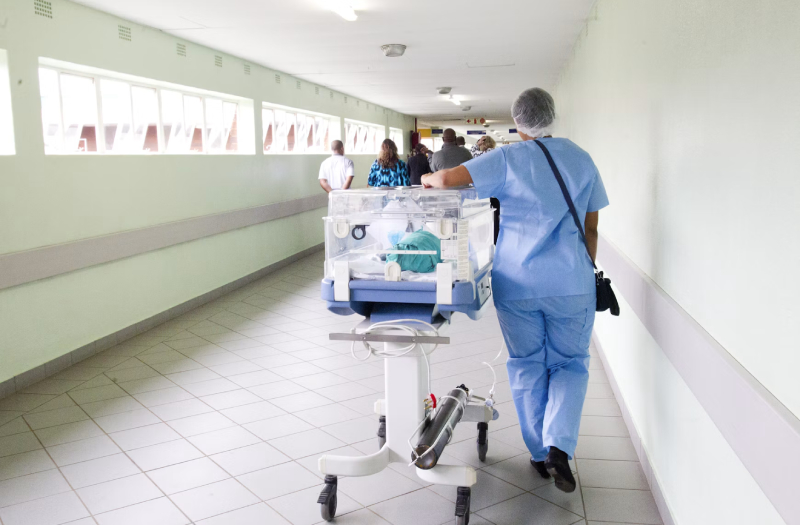 person-walking-on-hallway-in-blue-scrub-suit-near-incubator